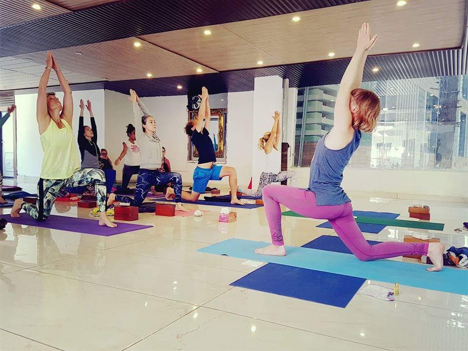 A room of students holding a low lunge with arms overhead